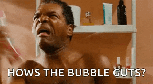 a shirtless man is brushing his teeth in front of a mirror in a bathroom and asking how the bubble guts .
