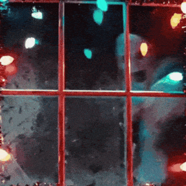 christmas lights are reflected in a window with a red trim
