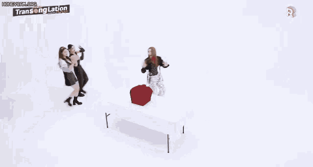 two women are dancing in front of a white background . one of the women is wearing a silver top .