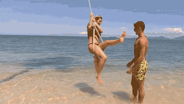 a woman in a bikini is swinging on a rope over the ocean