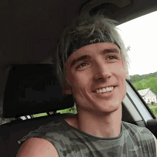 a young man wearing a headband is smiling while sitting in the back seat of a car