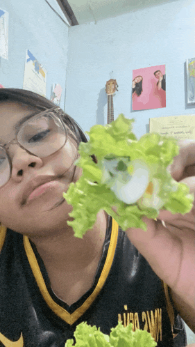 a girl wearing glasses holds a piece of lettuce