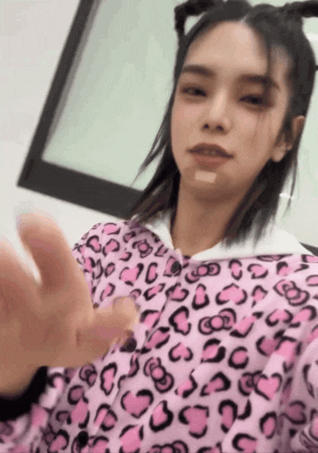 a woman wearing a pink leopard print shirt is waving at the camera