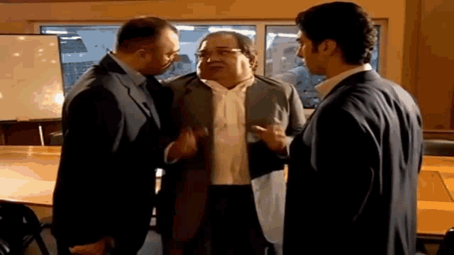 three men in suits are standing next to each other in a room .