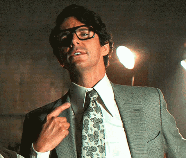 a man in a suit and tie is pointing at his neck