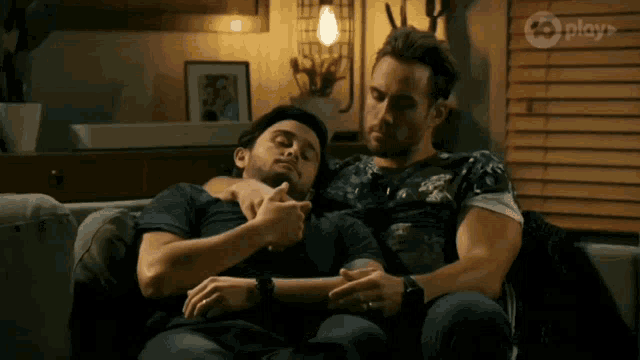 two men are hugging each other on a couch with play on the bottom