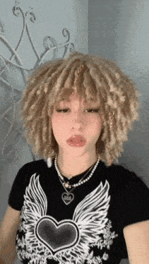a girl with curly hair is wearing a black shirt with wings and a heart necklace .