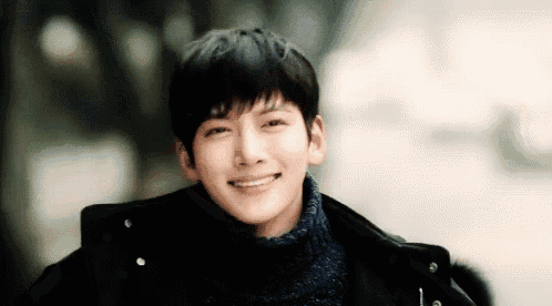 a young man wearing a black coat and a blue sweater is smiling .