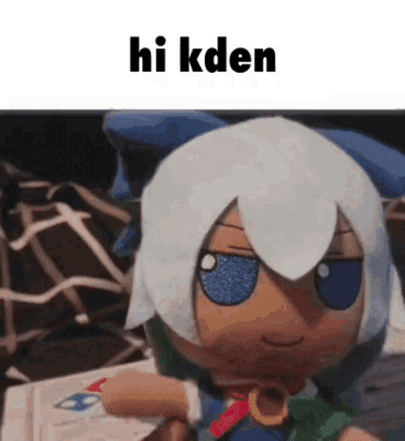 a stuffed doll with white hair and blue eyes is sitting on a couch with the words `` hi kden '' written above it .