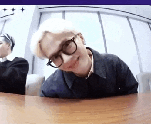 a man wearing glasses is sitting at a table with another man .
