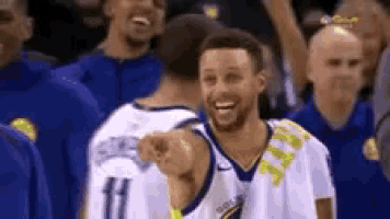 a basketball player is smiling and pointing at the camera while standing in front of a crowd .