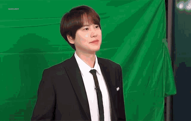 a man in a suit and tie is standing in front of a green screen and making a funny face .