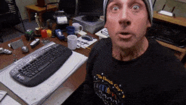 a man wearing a black shirt that says the electric city is sitting at a desk