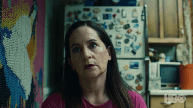 a woman in a pink shirt is sitting in front of a fridge that has stickers on it