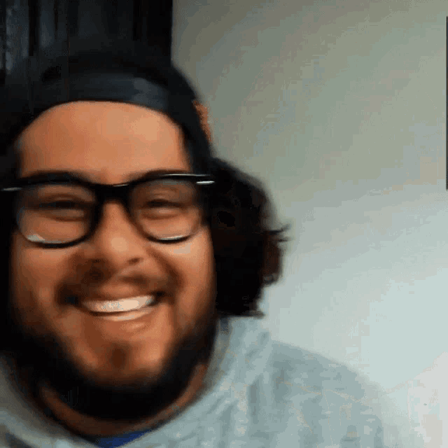 a man with a beard wearing glasses and a headband smiles