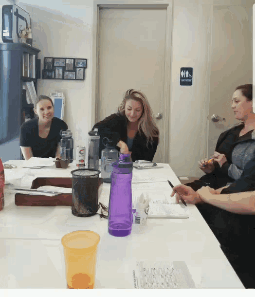 a group of people sitting around a table with a purple water bottle on it