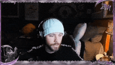 a man wearing a blue beanie and headphones is sitting in front of a computer screen with a purple frame around him .