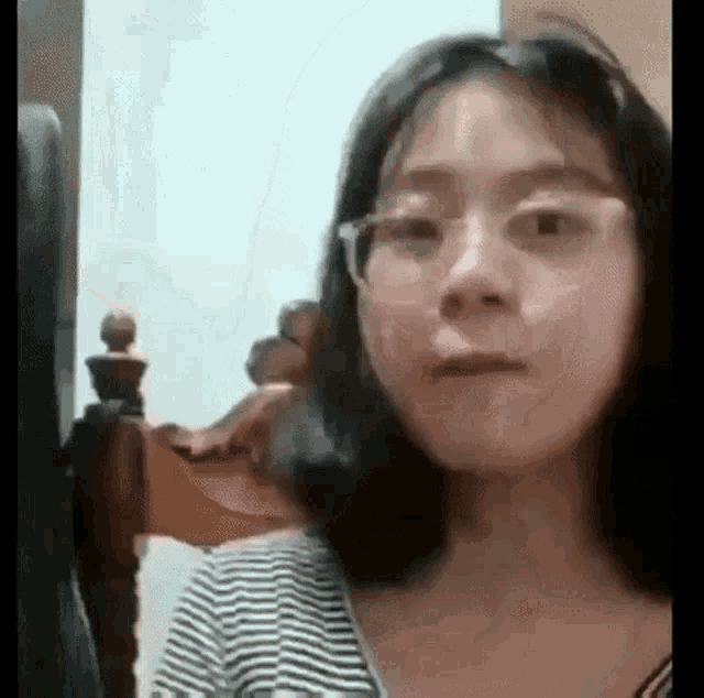 a young woman wearing glasses is making a funny face while sitting in front of a bed .