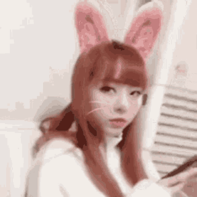 a girl with red hair and pink bunny ears is holding a cell phone in her hand .
