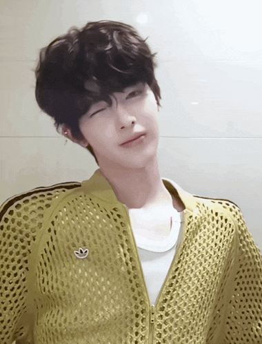 a young man wearing a yellow adidas jacket looks at the camera with his eyes closed