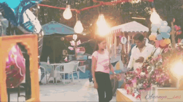 a woman in a pink shirt stands in front of a table with flowers