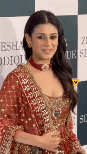 a woman in a red and gold dress is standing in front of a sign that says ' esha ' on it .