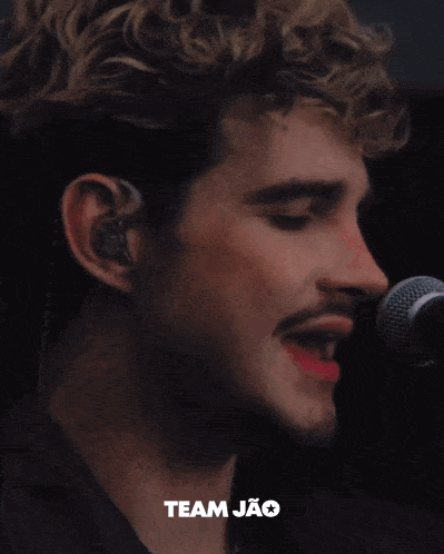a close up of a man singing into a microphone with the word team jao on the bottom right