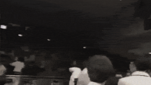 a black and white photo of a crowd of people dancing in a room .