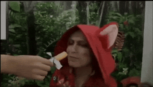 a woman in a red hood is being fed a piece of food by a man .