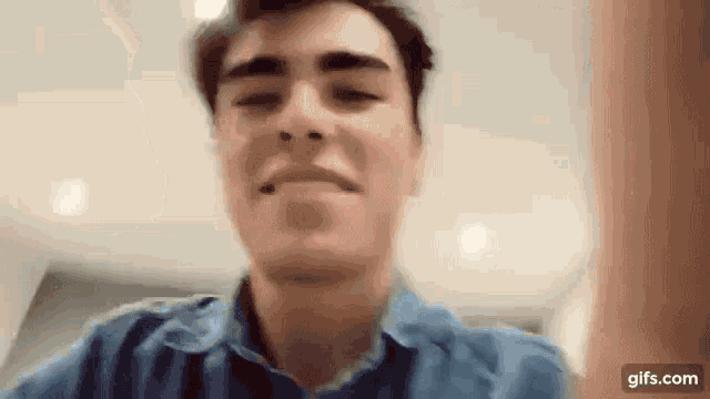 a young man in a blue shirt is making a funny face and looking at the camera .