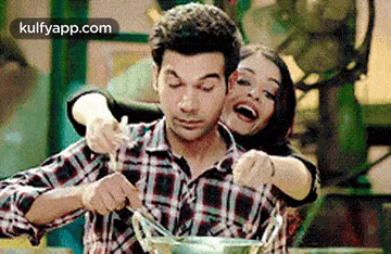a woman is hugging a man while he is cooking in a bowl .
