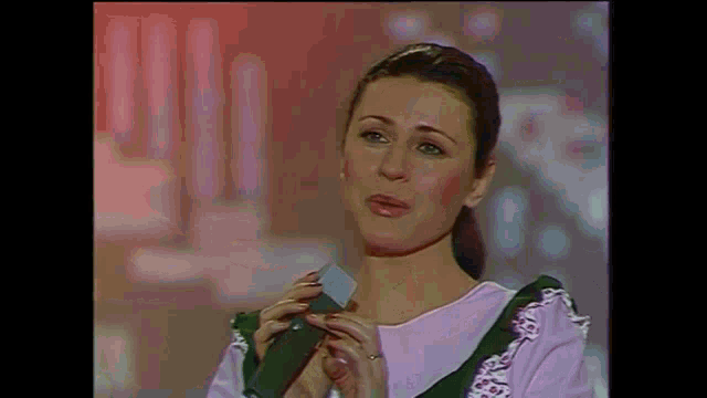 a woman is singing into a microphone while wearing a pink top