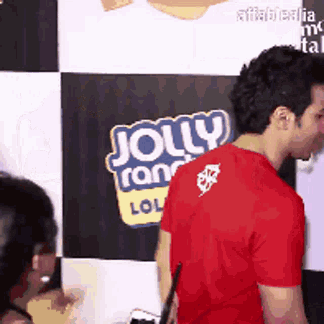 a man in a red shirt is standing in front of a jolly ranch lollipop sign