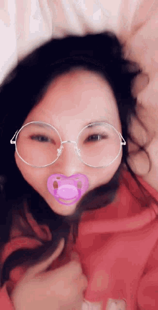 a woman wearing glasses and a pink pacifier in her mouth