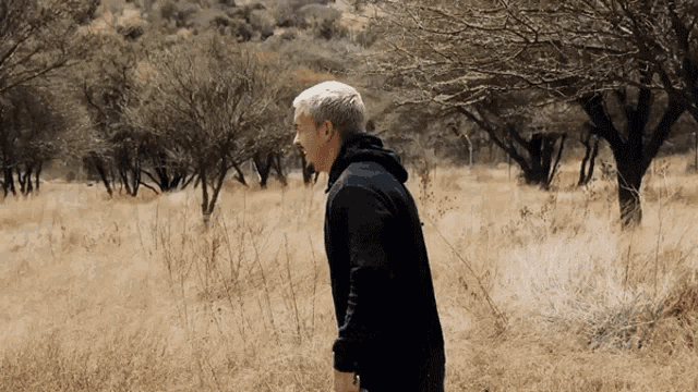 a man in a black jacket walks through a field
