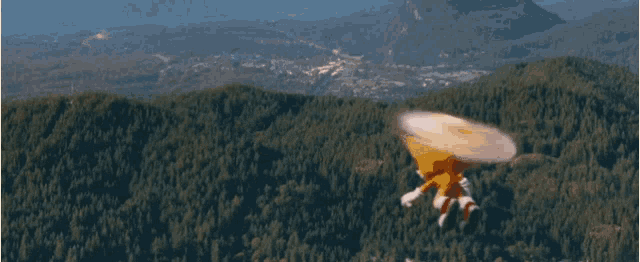 a stuffed animal is flying through the air over a forest with mountains in the background