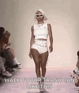 a woman is walking down a runway at a fashion show wearing shorts and a tank top .