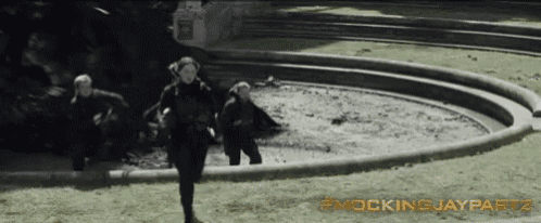 a group of people running around a fountain with the words mockingjaypart2 on the bottom