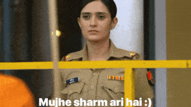 a woman in a police uniform stands behind a yellow fence with the words " mujhe sharm ari hai " written below her
