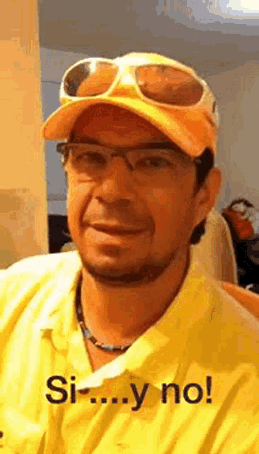 a man wearing a yellow shirt , sunglasses and a baseball cap is smiling .