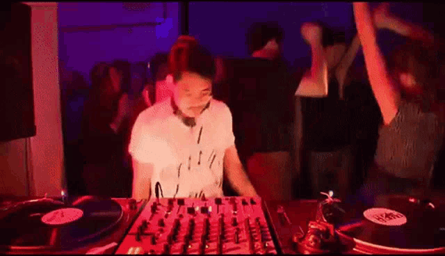 a dj is playing music at a party in a dark room while people dance in the background .