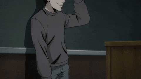 a man in a grey sweater is standing in front of a blackboard with his hand on his forehead