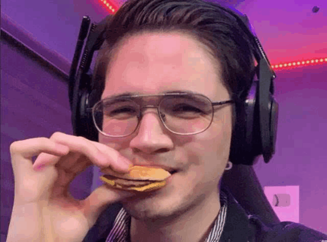 a man wearing glasses and headphones is eating a piece of food .