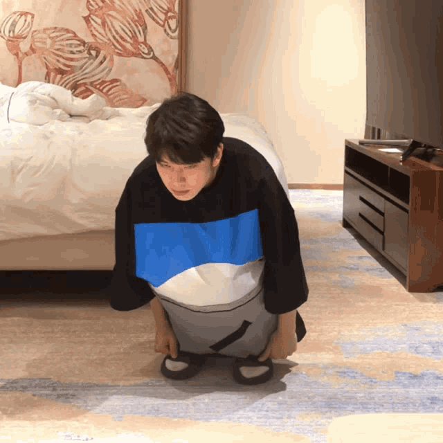 a man wearing a blue and white shirt is squatting down
