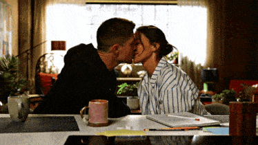 a man and a woman kissing at a table with a pink mug
