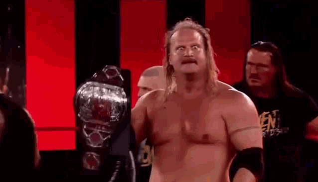 a shirtless wrestler is holding a world heavyweight championship belt in a ring .