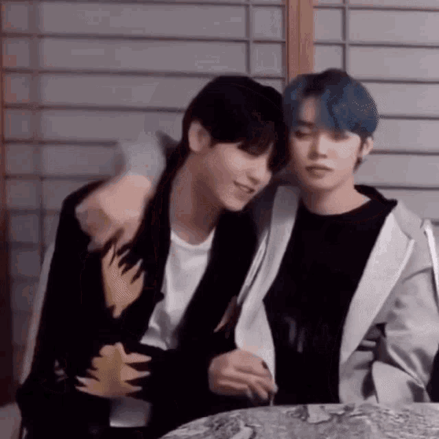 two young men are sitting next to each other at a table and hugging .