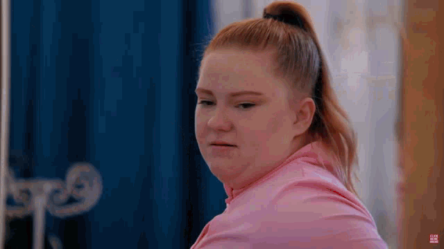 a woman in a pink shirt with a ponytail is making a funny face .