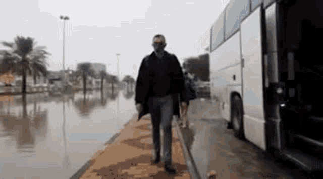 a man wearing a mask is walking across a flooded street next to a bus .