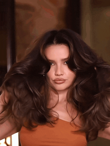 a woman with long dark hair is wearing a brown top